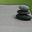 Zdjęcie przedstawiające otwartą książkę i ułożone na niej trzy kamienie